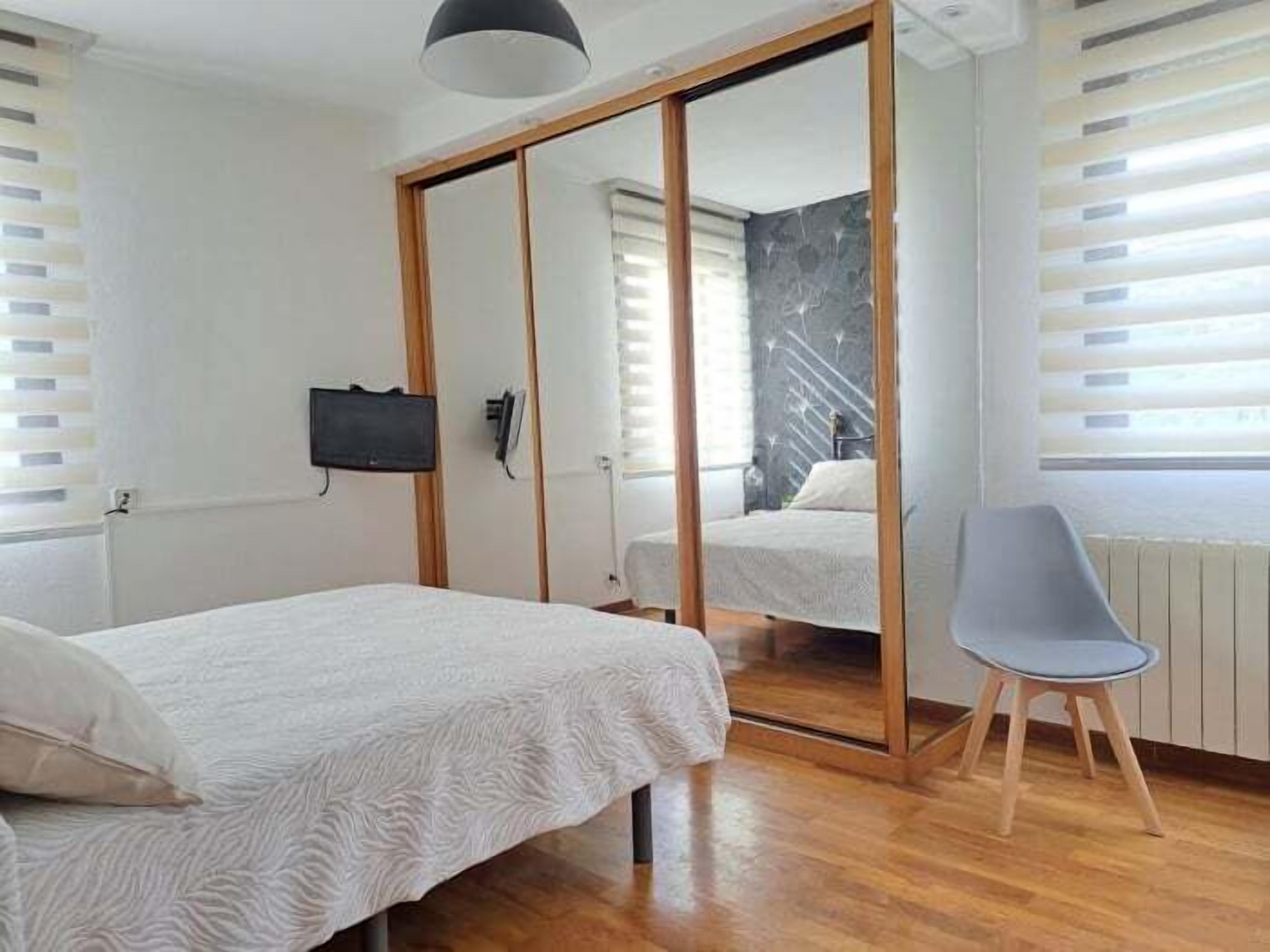 A bedroom with a bed, a chair, a mirror, and a TV.
