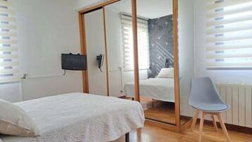 A bedroom with a bed, a chair, a mirror, and a TV.