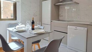 Een moderne keuken met een ingebouwde vaatwasser, een eettafel gedekt voor twee personen en een raam met zonwering.