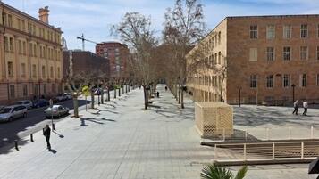 Un amplio paseo peatonal bordeado de árboles y bancos, flanqueado por edificios con grandes ventanales y un cielo despejado.