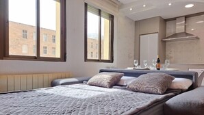 Een slaapkamer met een bed, een raam, een nachtkastje en uitzicht op gebouwen.