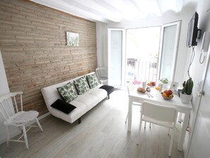 A bright room with a white sofa, a dining table with fruit and a cactus, and a brick wall.