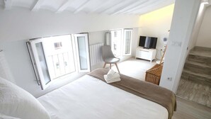 Et hotelværelse med en stor seng, et fjernsyn, en stol og en trappe.