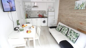 En kompakt opholdsstue med tekøkken, spiseplads og en sofa med mønstrede puder.