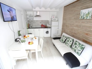Un espacio habitable compacto con kitchenette, comedor y un sofá con cojines estampados.