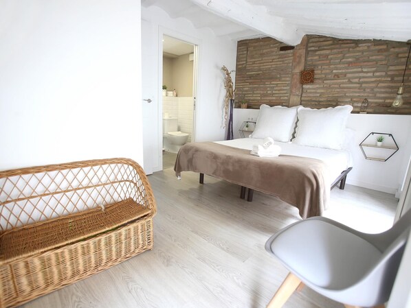 A bedroom with a bed, a chair, a wicker basket, and a brick wall.