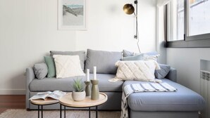 Een moderne woonkamer met een grijze bank, een klein rond tafeltje met kaarsen en een groot raam.