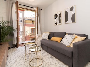 Un salon avec un canapé gris, deux petites tables rondes en verre, une plante en pot et un balcon avec vue.