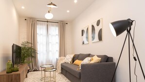 A modern living room with a grey sofa, a standing floor lamp, a TV on a wooden stand, and a potted plant. - Los apartamentos de Elena, centro histórico I by El Rincon (Logroño)