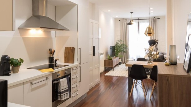 A modern kitchen with white cabinetry, a stainless steel range hood, and a dining area with a wooden table and chairs. - Los apartamentos de Elena, centro histórico I by El Rincon (Logroño)