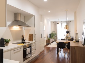Une cuisine moderne avec des meubles blancs, une hotte en acier inoxydable et un coin repas comprenant une table et des chaises en bois.