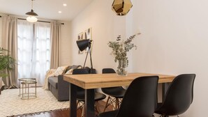 A modern living room with a wooden dining table, black chairs, a sofa, and a potted plant. - Los apartamentos de Elena, centro histórico I by El Rincon (Logroño)