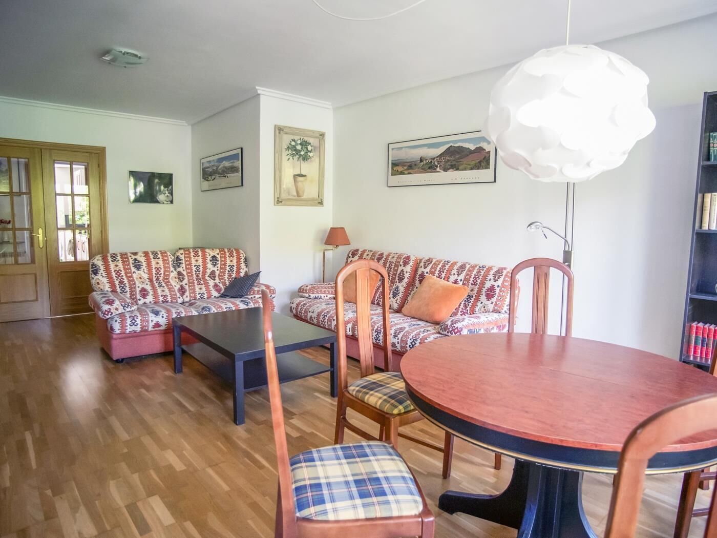 Ein Wohnzimmer mit gemusterten Sofas, einem runden Holztisch und einem Bücherregal.
