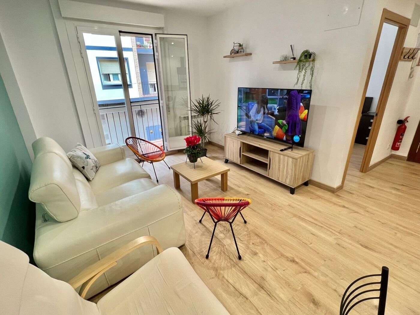 A modern living room with a sofa, two chairs, a coffee table, a TV, and a balcony with a view.