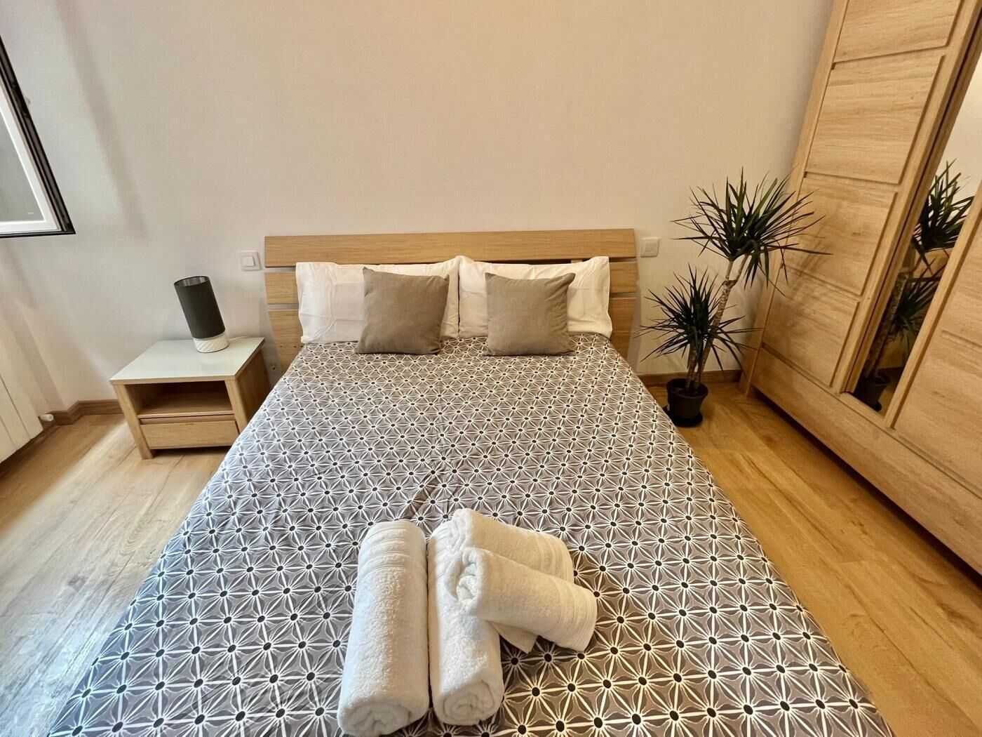A neatly made bed with a geometric patterned bedspread, two pillows, and two rolled towels on the bed.