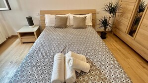 Una cama bien hecha con una colcha de estampado geométrico, dos almohadas y dos toallas enrolladas sobre la cama.