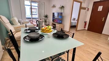 Ruokailutila, jossa on kahdelle katettu pöytä, sohva, televisio ja ovi, jonka yläpuolella on kyltti, jossa lukee ”ULOSKÄYNTI”.