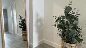 A hallway with a mirror reflecting a plant in a wicker basket, a door, and a light-colored floor. - Apartment La Paz, new, wifi & confort by El Rincon (Logroño)
