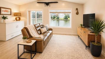 A living room with a leather sofa, a coffee table, a TV, a cabinet, and a large window with a view of a body of water.