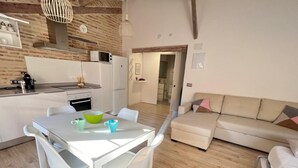 Una cucina moderna con elettrodomestici bianchi, un tavolo da pranzo con sedie e un divano beige nella zona living.