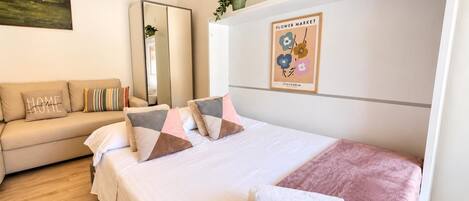 Una habitación de hotel con cama, sofá, espejo, una obra de arte en la pared y una planta en maceta.