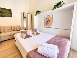 A hotel room with a bed, a sofa, a mirror, a wall art piece, and a potted plant. - Loft Laurel acogedor (Logroño)