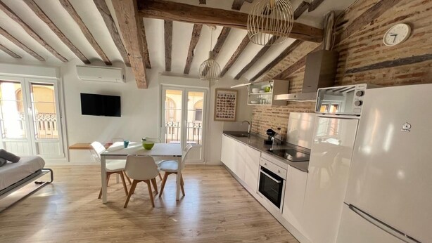 Una cucina moderna con travi in legno, un'area pranzo con tavolo e sedie, e un frigorifero bianco.