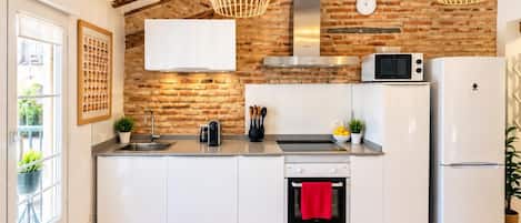 Una cocina moderna con paredes de ladrillo visto, vigas de madera, una campana de acero inoxidable, microondas, refrigerador y un comedor con mesa y sillas.