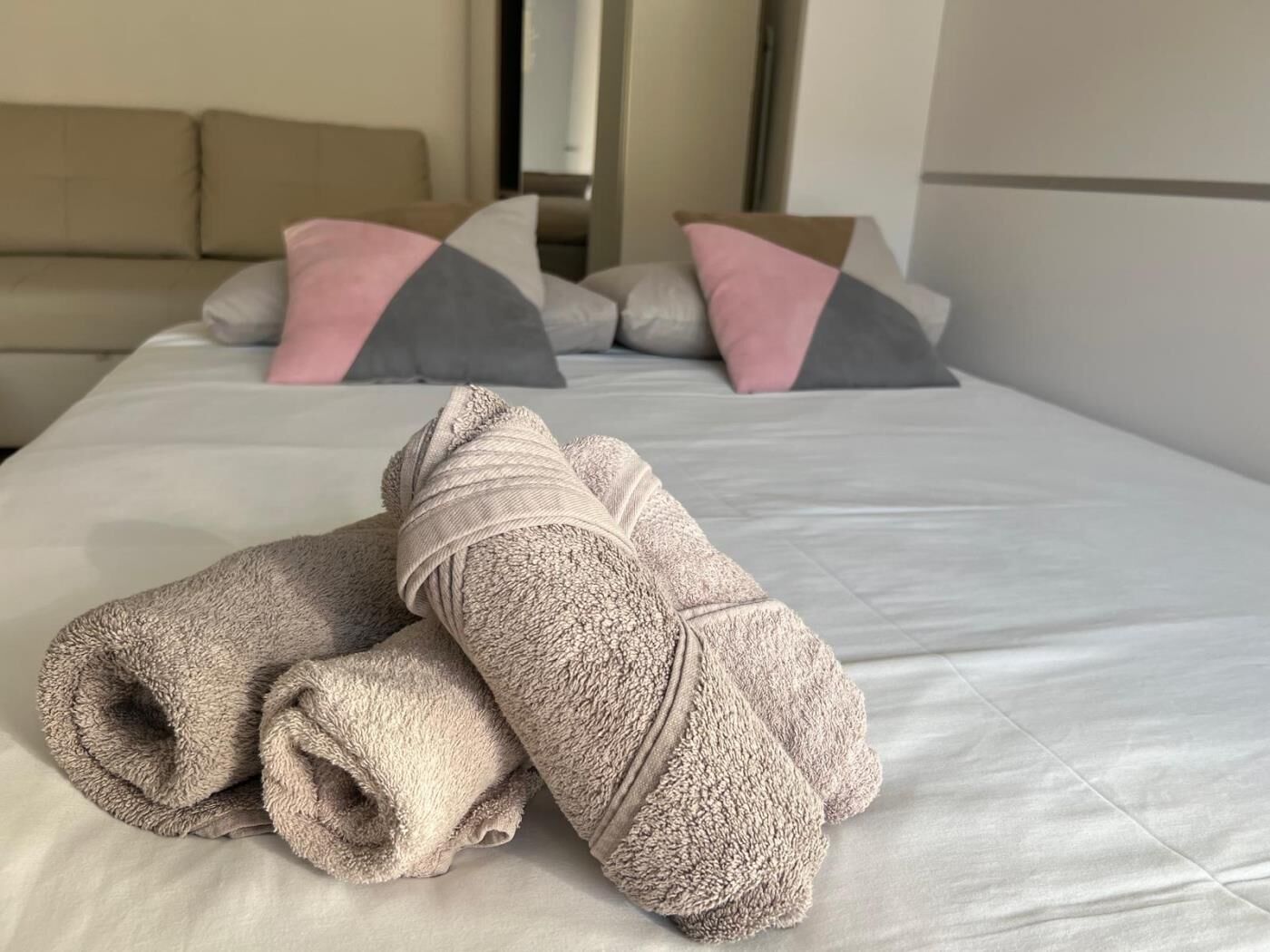 Un lit bien fait, avec des serviettes pliées, un canapé agrémenté de coussins à motifs et un mur uni.