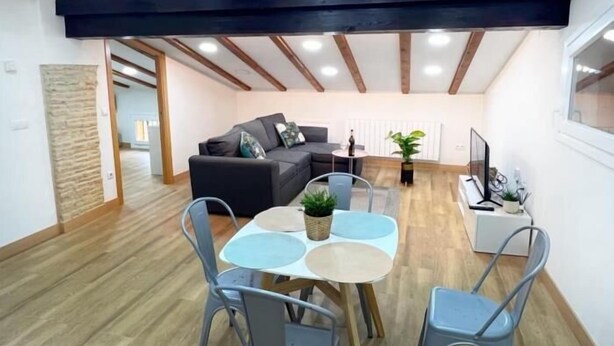 A spacious living area with a sofa, dining table, and chairs, wooden beams on the ceiling, and a view into another room. - El Rincón del Marqués by El Rincon (Logroño)