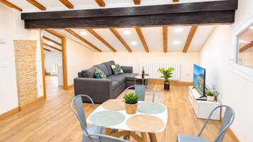 Una sala de estar moderna con sofá, mesa de comedor con sillas, planta en maceta y televisor.