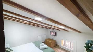 Un dormitorio con dos camas, techo de madera, un radiador, un televisor y una ventana con persianas.