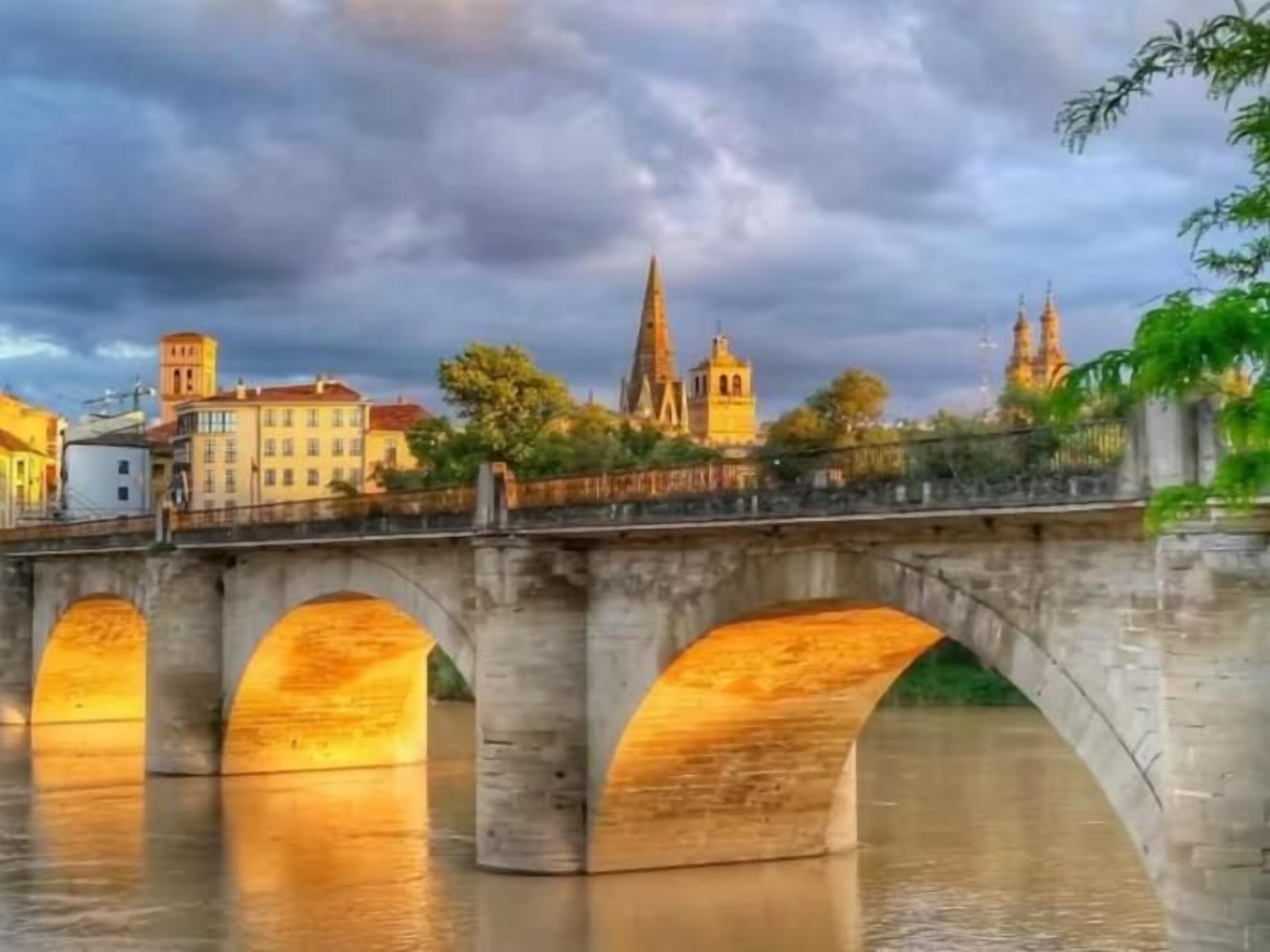 A stone bridge over water with a cityscape in the background.