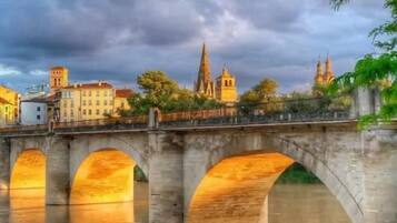 A stone bridge over water with a cityscape in the background.