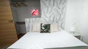 A hotel room with a bed, a green bedspread, two pillows, a white towel, a nightstand with a lamp, a wardrobe, and a wall-mounted clock. - El Rincón del Marqués by El Rincon (Logroño)