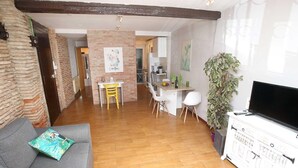 A living room with a sofa, a dining area with chairs, a TV, and a kitchen in the background. - RINCON DEL MARQUES ENTRESUELO (Logroño)