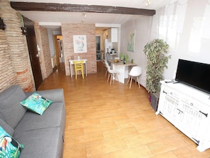 Un salon avec un canapé, un coin repas avec des chaises, un téléviseur et une cuisine à l’arrière-plan.