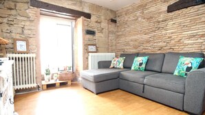 A living room with a stone wall, a grey sectional sofa, and a wooden floor. - RINCON DEL MARQUES ENTRESUELO (Logroño)
