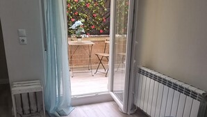 Een slaapkamer met een bed, een radiator, een raam met gordijnen, en uitzicht op een terras met een tafel en stoelen.