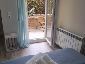 Une chambre avec un lit, un radiateur, une fenêtre avec des rideaux et une vue sur une terrasse extérieure avec une table et des chaises.