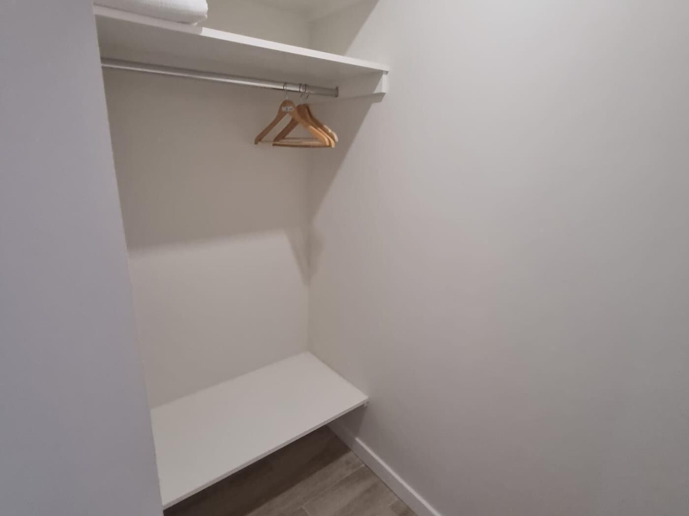Un placard avec un cintre en bois, une étagère et un rouleau de papier toilette.