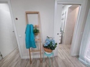 Un couloir avec une échelle en bois appuyée contre un mur, un panier contenant une plante et une serviette bleue accrochée à l’échelle.