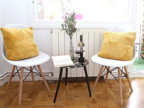 Dos sillas blancas con cojines amarillos, una mesita con un libro, una copa de vino y un florero con flores.