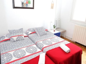 Un dormitorio con dos camas, una mesita de noche, una planta pequeña y una ventana.