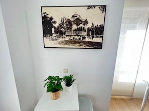 Fotografía en blanco y negro enmarcada de un pabellón, una pequeña mesa con dos plantas en macetas y un interruptor de luz en la pared.