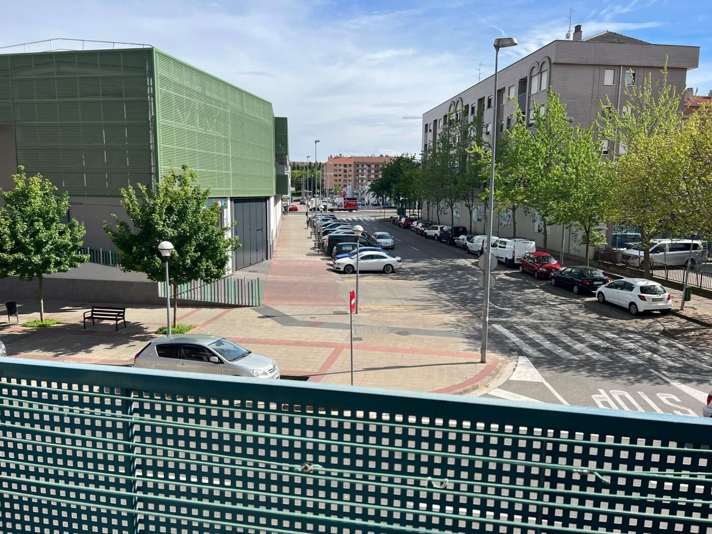A street view with parked cars, a green building, and a pedestrian crossing.