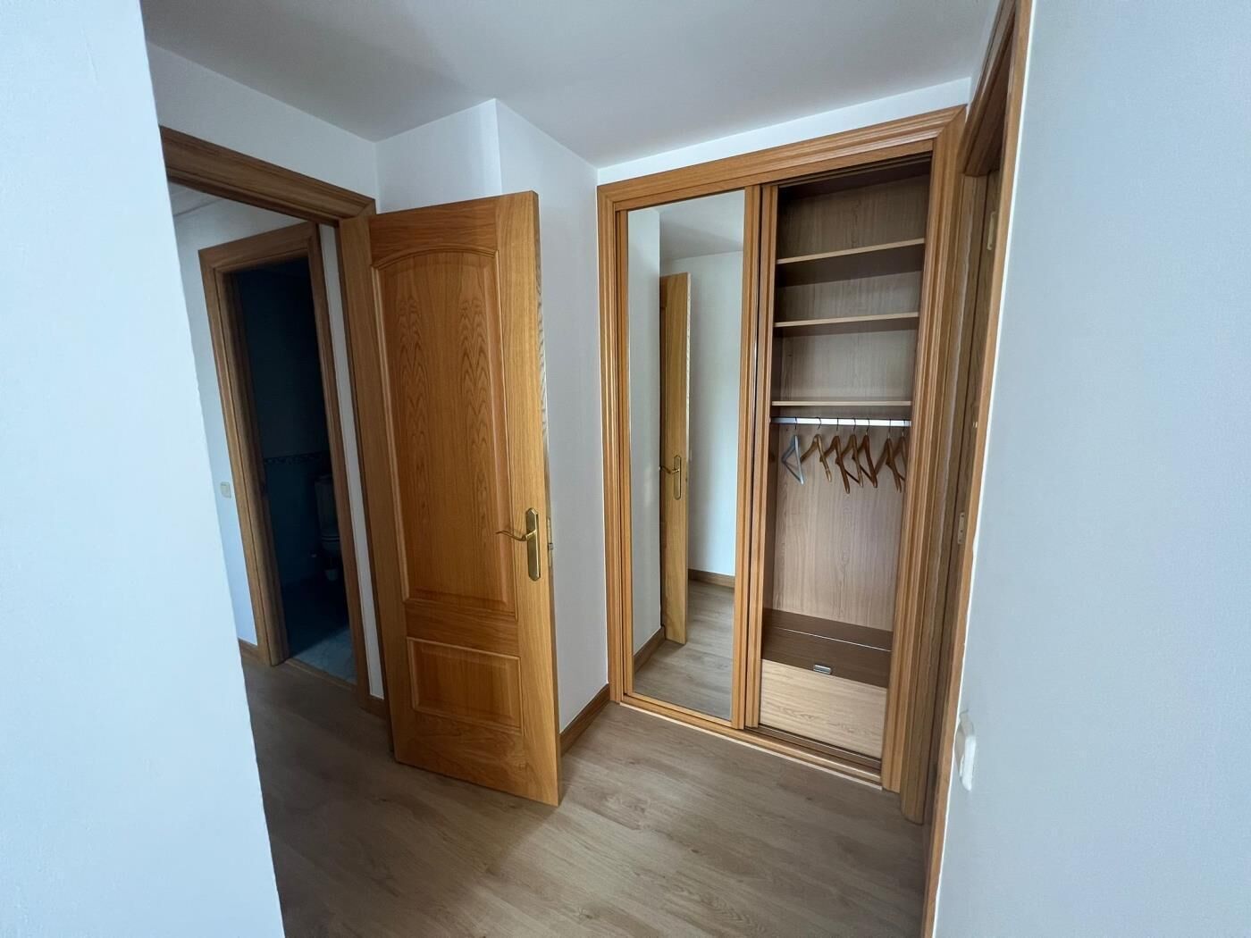 Una habitación con un armario de madera, un espejo y una puerta que da a otra estancia.