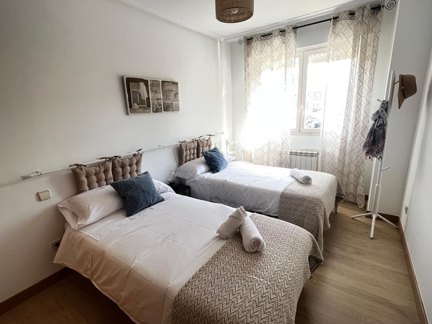 Un dormitorio con dos camas, un radiador, una ventana con cortinas y un perchero.