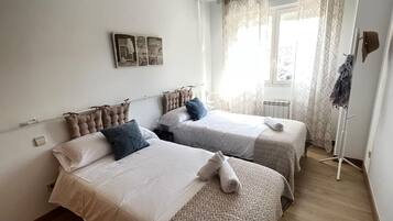 Un dormitorio con dos camas, un radiador, una ventana con cortinas y un perchero.