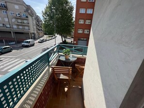 Un balcón con vistas a la calle, una planta en maceta y una pequeña mesa.
